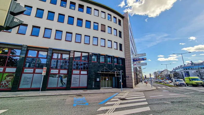 Modernes Bürogebäude an einer Straßenecke mit großen Fenstern und einer dunklen Fassadenverkleidung.