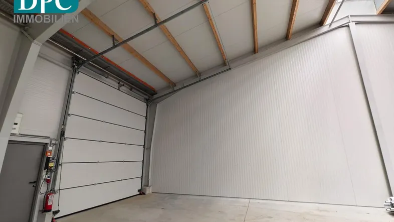 Geräumige Lagerhalle mit hohen Decken, Rolltor und viel Tageslicht durch Oberlichter.