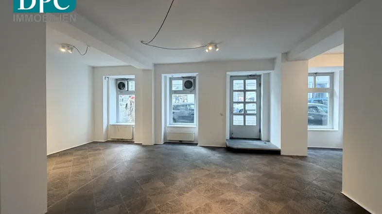 Geräumiger, leerer Geschäftsraum mit großen Fenstern und dunklen Fliesen, bereit zur individuellen Gestaltung.