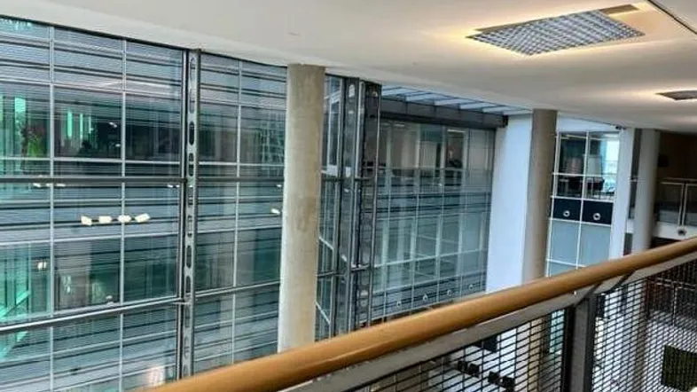 Moderner Innenbereich mit hohen Glasfassaden und Blick auf weitere Etagen, beleuchtet durch Deckenleuchten.