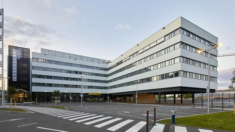 Modernes Bürogebäude mit markanter Architektur, großen Fensterfronten und einem weitläufigen Parkplatzbereich.