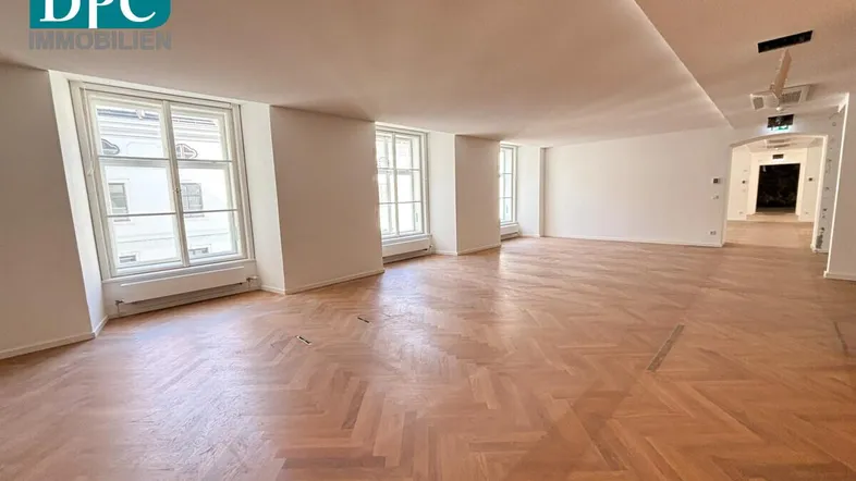 Geräumiger, heller Innenraum mit Fischgrätparkett und großen Fenstern, ideal für Wohn- oder Büronutzung.