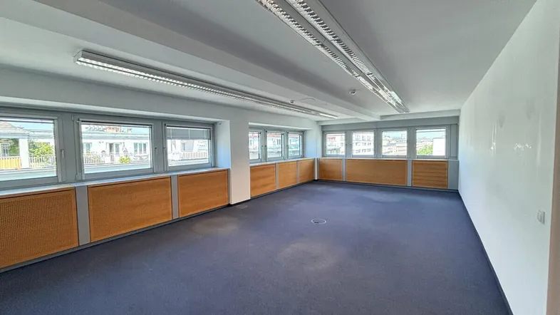 Geräumiges Büro mit großen Fenstern, Teppichboden und Holzpaneelen, ideal für gewerbliche Nutzung.