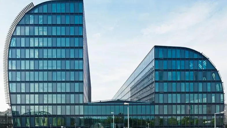 Modernes Bürogebäude mit geschwungener Glasfassade und einer Fußgängerbrücke im Vordergrund.