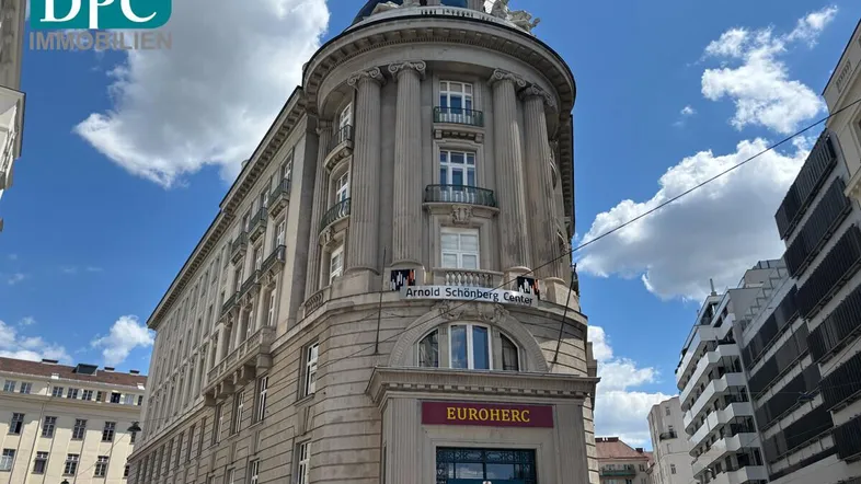 Historisches Eckgebäude mit imposanter Architektur und Säulenfassade unter blauem Himmel.