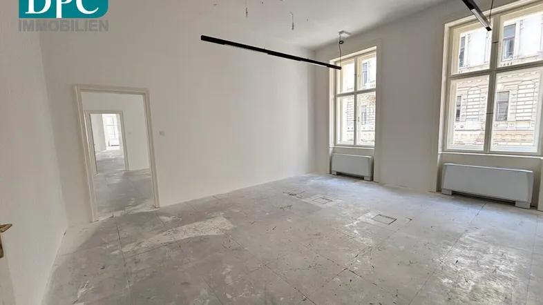 Geräumiger, heller Gewerberaum mit hohen Decken, großen Fenstern und unfertigem Betonboden, bereit für den Ausbau.