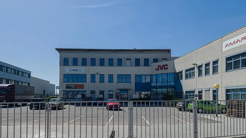 Außenansicht eines modernen Geschäftsgebäudes mit großem Parkplatz und blauer Beschilderung unter klarem Himmel.