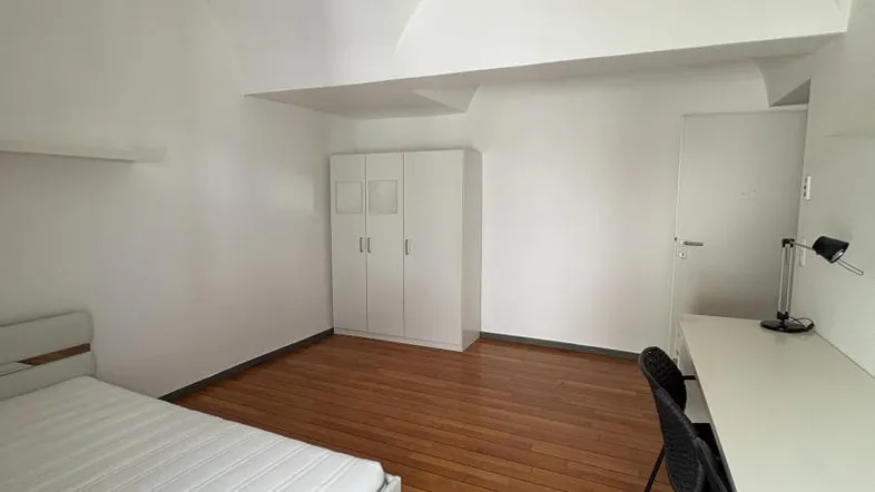 Helles Schlafzimmer mit Holzboden, gewölbter Decke und einfacher Einrichtung.