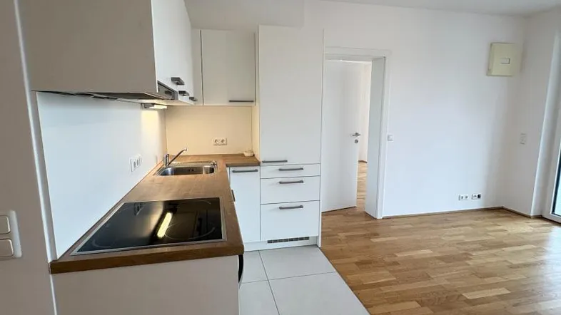 Moderne Einbauküche mit weißen Schränken und Holzarbeitsplatte, angrenzend an einen Wohnbereich mit Parkettboden.