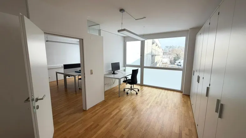 Helles Büro mit Holzfußboden, großen Fenstern und integrierten Schränken, bietet viel Stauraum.