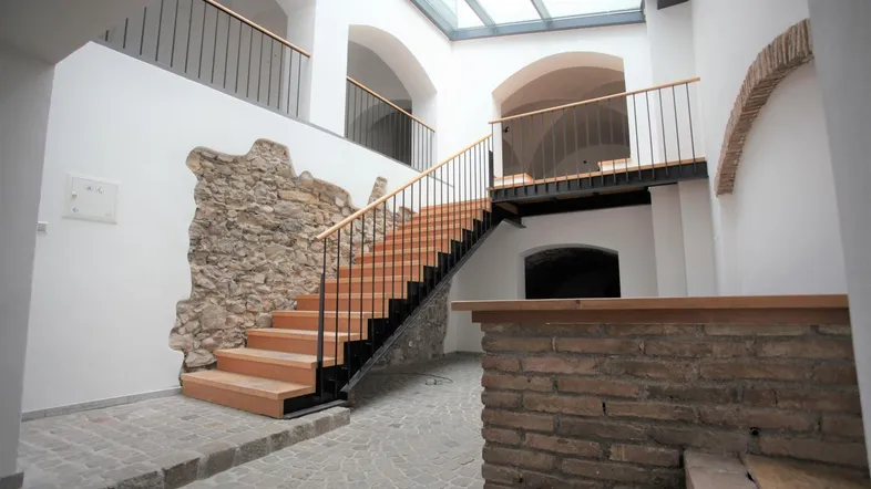 Geräumiges Treppenhaus mit Holzstufen, Steinmauerelementen und einem Glasdach, das viel Tageslicht hereinlässt.