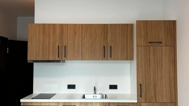 Moderne Küchenzeile mit Holzfronten, weißer Arbeitsplatte und integrierten Geräten.