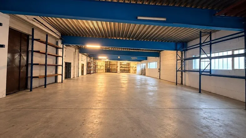 Geräumige Lagerhalle mit Betonboden, blauen Stahlträgern und hohen Decken, bereit zur Nutzung.