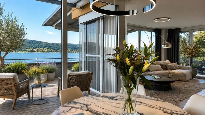 Heller Wohn- und Essbereich mit Marmortisch, modernen Leuchten und Zugang zur Terrasse mit Seeblick.