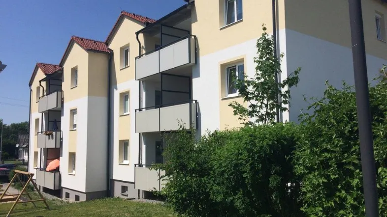 Mehrfamilienhaus mit gelb-weißer Fassade, roten Dächern und mehreren Balkonen in sonniger Umgebung.