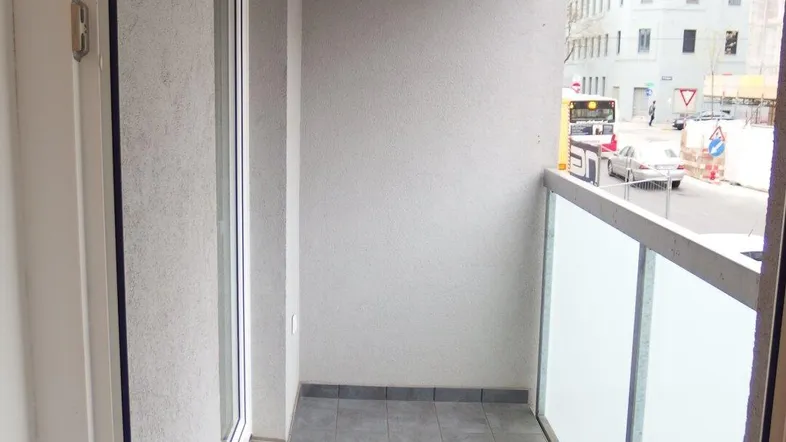 Heller Balkon mit Fliesenboden und Glasbrüstung, bietet einen Blick auf die Stadtstraße.