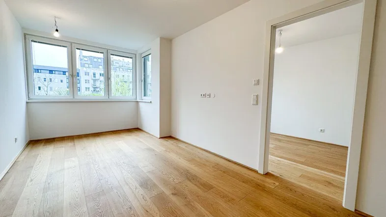 Helles, leeres Zimmer mit großen Fenstern und neuem Holzparkettboden, bereit zum Einzug.