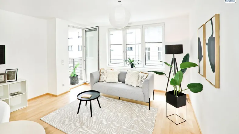 Helles Wohnzimmer mit modernem Sofa, Holzboden und Zugang zum Balkon.