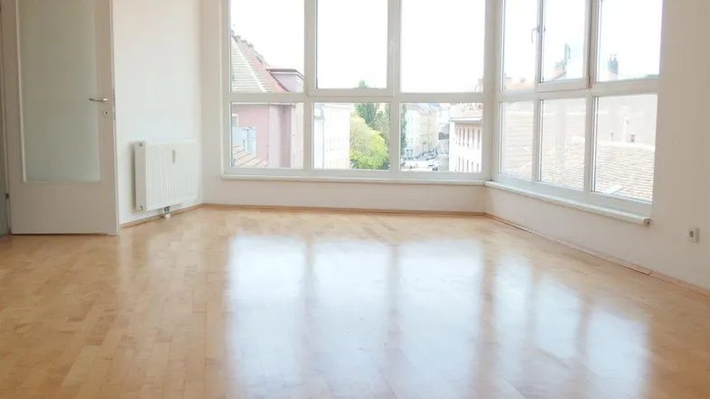 Helles Wohnzimmer mit Parkettboden und großen Fenstern, die viel Tageslicht hereinlassen.