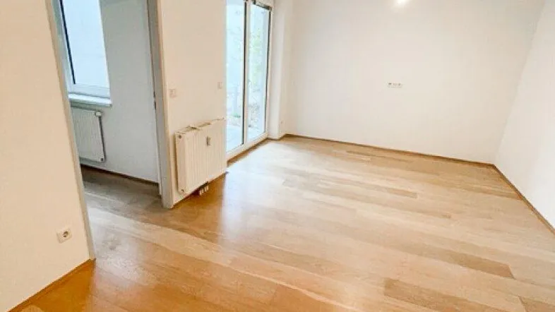 Heller Wohnbereich mit neuwertigem Holzfußboden und Zugang zu einem weiteren Raum sowie zur Terrasse.