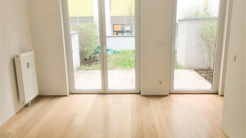 Heller Wohnraum mit hellem Holzboden, weißen Wänden und großen Fenstertüren zum Garten.
