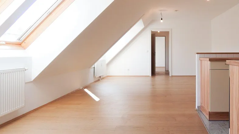 Helles Dachgeschosszimmer mit Holzboden und Dachfenstern, offen zu einem weiteren Bereich.