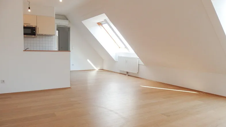 Helles Dachgeschosszimmer mit Holzboden und integrierter Küchenzeile, durch Dachfenster gut belichtet.