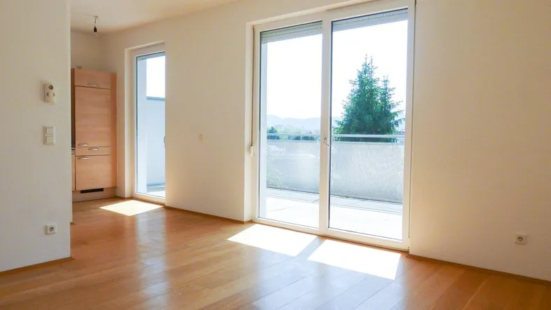 Helles Wohnzimmer mit Holzboden und großem Schiebefenster, das Zugang zu einem Balkon bietet.