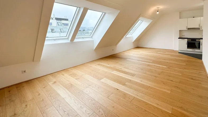 Helles Dachgeschoss-Wohnzimmer mit Holzboden und großen Dachfenstern, offen zur Küche.