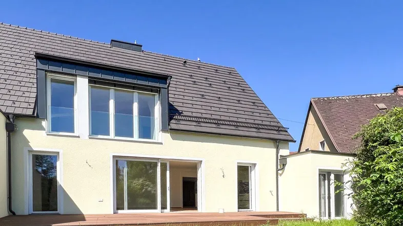 Moderne Hausrückseite mit großer Holzterrasse und Zugang zum Garten unter blauem Himmel.