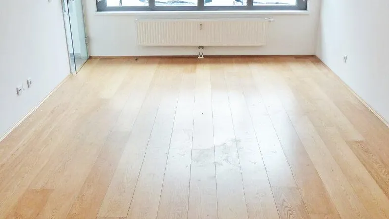 Helles, leeres Zimmer mit Holzfußboden und großen Fenstern, bereit zur individuellen Gestaltung.