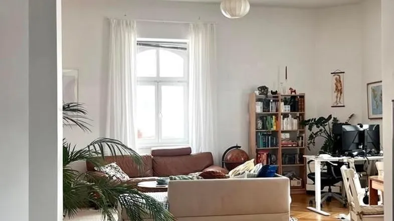 Geräumiges Wohnzimmer mit Fischgrätparkett, bequemen Sofas und einem Arbeitsbereich am Fenster.