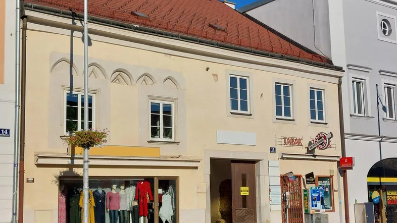 Historisches Gebäude mit Ladenlokal im Erdgeschoss und Wohnungen darüber, gekennzeichnet durch ein rotes Ziegeldach und traditionelle Fenster.