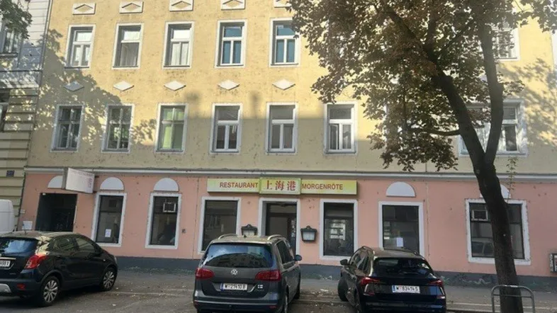 Gebäudefassade mit Restaurant im Erdgeschoss und geparkten Autos davor auf der Straße.
