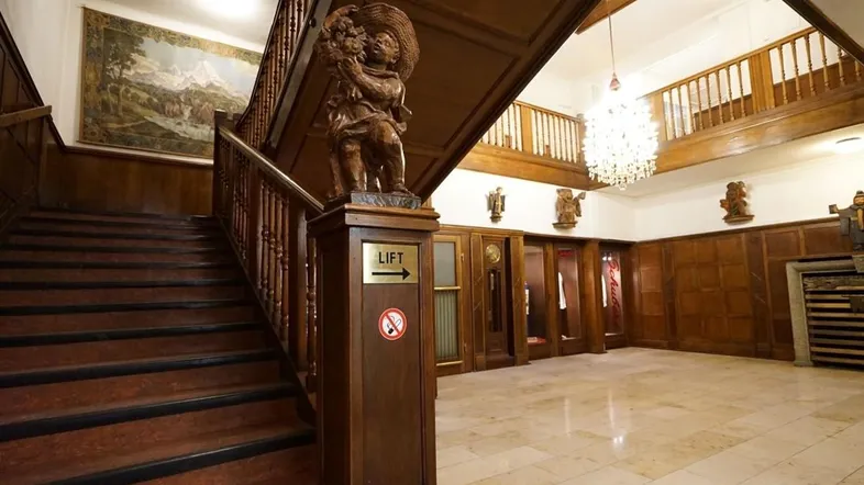 Großzügiges Treppenhaus mit eleganter Holztreppe, Marmorboden und einem antiken Kronleuchter.