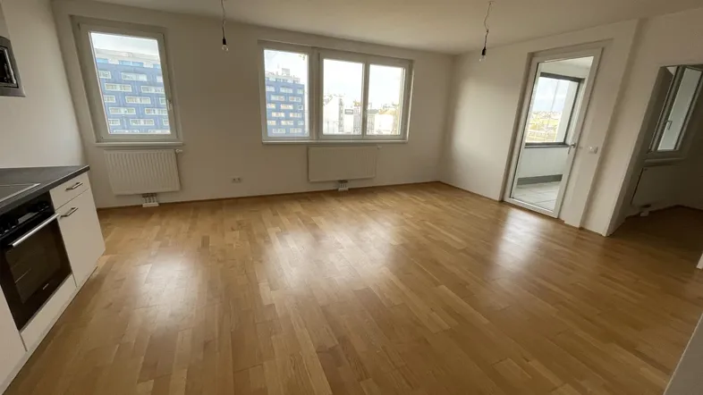 Helles Wohnzimmer mit Parkettboden, großen Fenstern und Zugang zu einem Balkon.