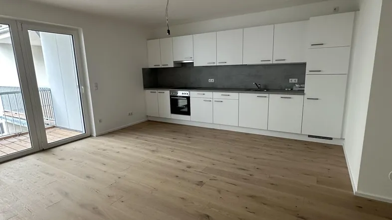 Helles, offenes Wohnzimmer mit integrierter Küche, Parkettboden und Zugang zum Balkon.