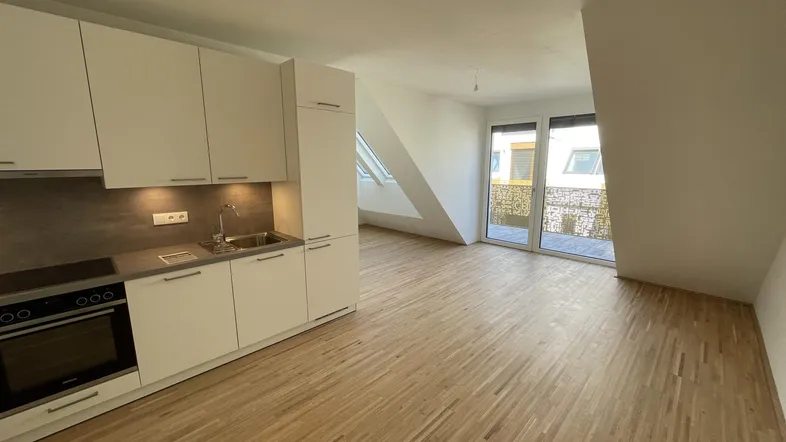 Moderne Einbauküche in einem hellen Raum mit Holzboden, Dachschrägen und Zugang zu einem Außenbereich.