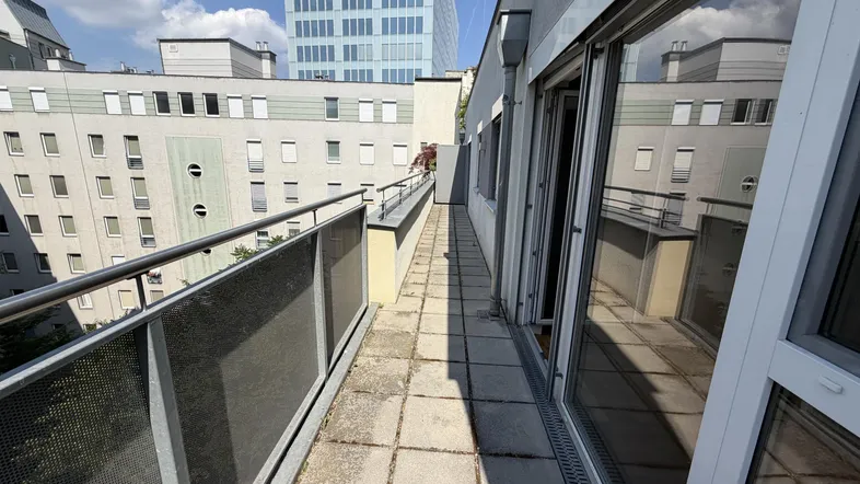 Langer, schmaler Balkon mit Fliesenboden und Blick auf die umliegenden Gebäude und einen modernen Wolkenkratzer.