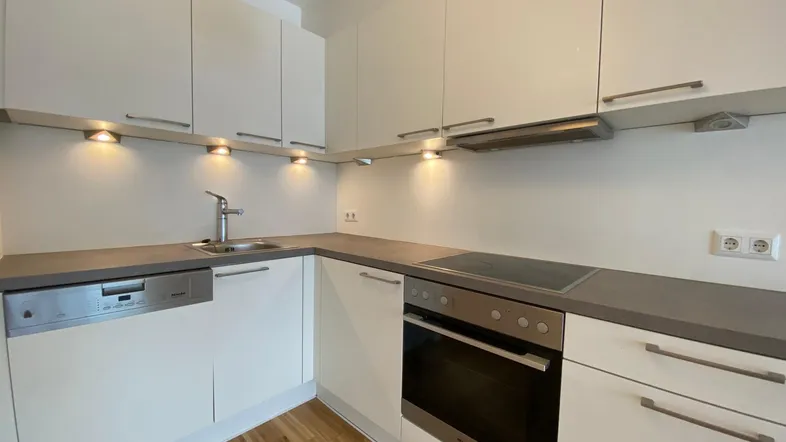 Moderne Einbauküche mit weißen Schränken, grauer Arbeitsplatte und integrierten Geräten.