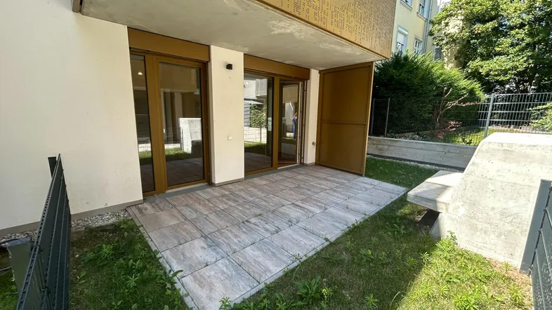 Große gepflasterte Terrasse mit angrenzender Rasenfläche und Zugang zu den Innenräumen.