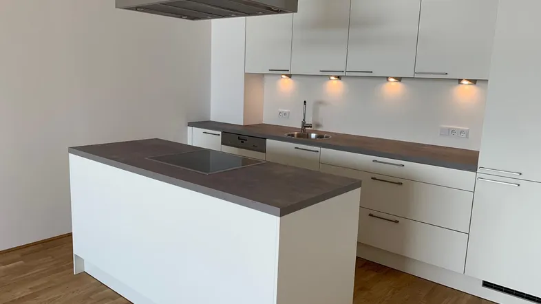Moderne Einbauküche mit Kochinsel, Induktionskochfeld und Dunstabzugshaube in hellem Design.