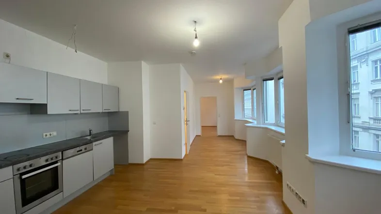 Heller offener Wohnbereich mit integrierter Küche, Parkettboden und großen Fenstern mit Stadtblick.