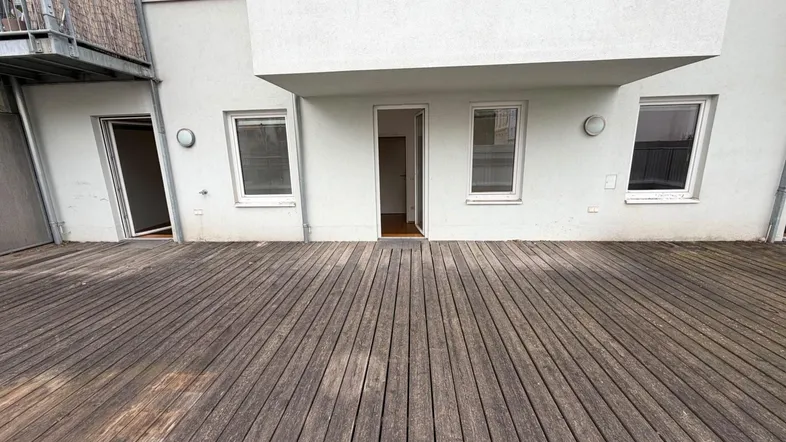 Große Holzterrasse mit direktem Zugang zu mehreren Räumen des Gebäudes und viel Platz im Freien.