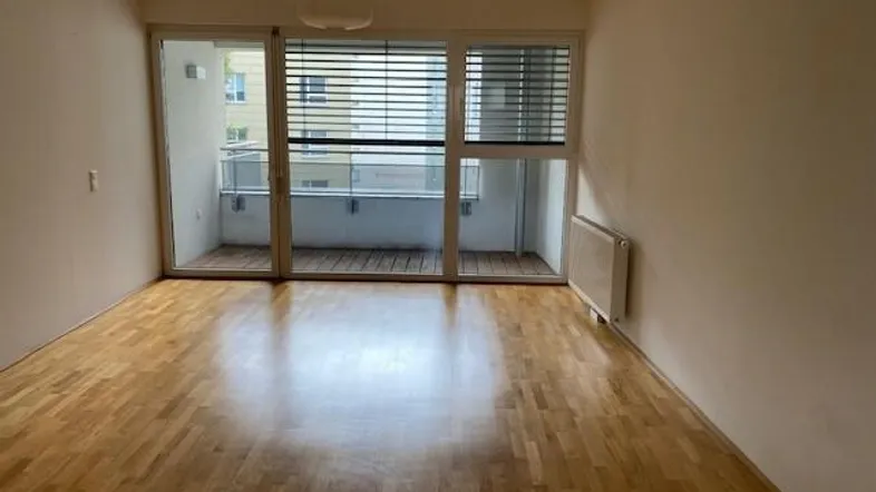 Heller Wohnraum mit Holzboden und großem Zugang zu einem Balkon, unmöbliert.