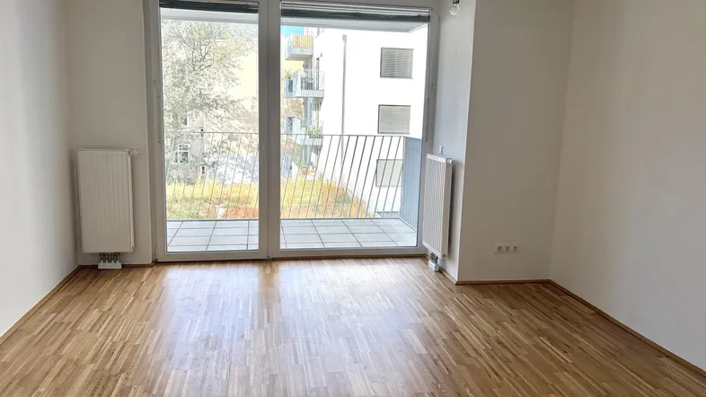Helles, leeres Zimmer mit Parkettboden und Zugang zu einem Balkon, ideal als Wohnbereich.