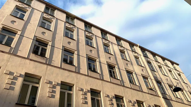 Altes Mehrfamilienhaus mit vielen Fenstern und klassischer Fassadengestaltung unter bewölktem Himmel.