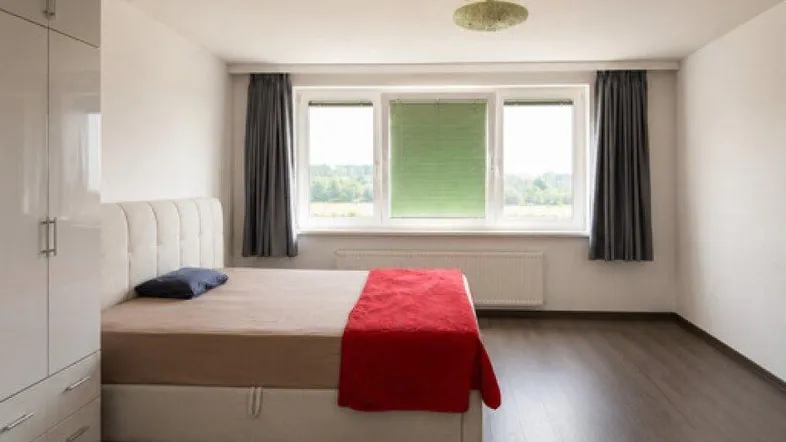 Helles Schlafzimmer mit Laminatboden, großem Fenster und weißem Kleiderschrank.