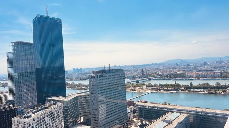 Panoramablick auf die Stadt mit modernen Hochhäusern, Fluss und Bergen im Hintergrund.