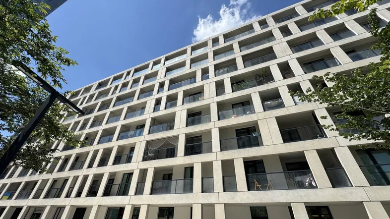 Moderne Wohngebäude-Fassade mit vielen Balkonen und großen Fenstern unter blauem Himmel.